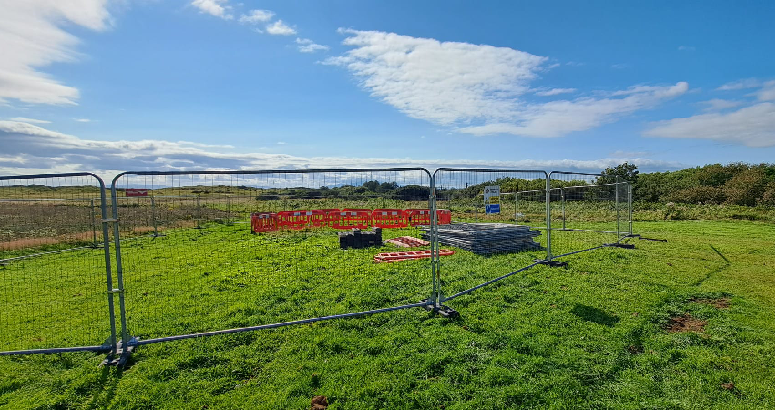 Fenced off area in grassy field. Blue sky overhead.